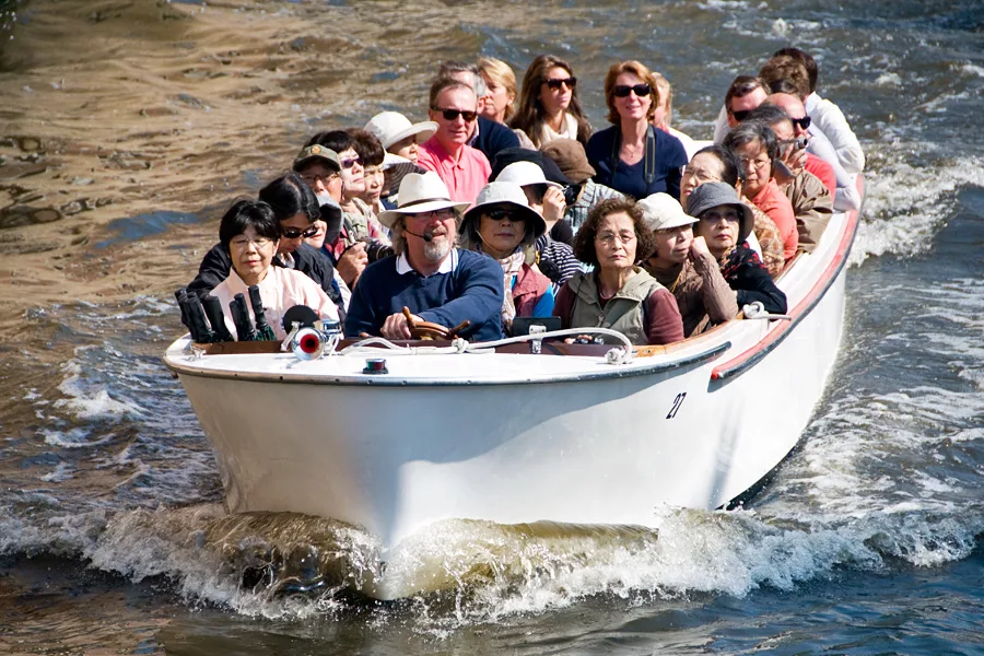 Туристы плыли по озеру на лодке. Экскурсионная лодка. Человек в лодке. Прогулка на лодке. Много людей в лодке.